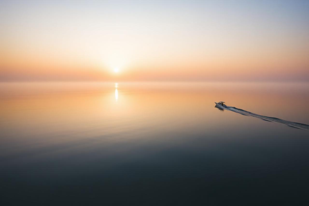 Glassy sunrise water off Naples with a single small boat wake