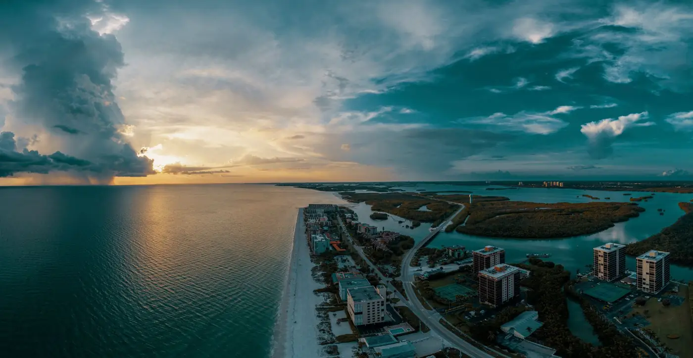 Naples Pier reaching into the turquoise Gulf of Mexico at sunset, with a yacht passing offshore